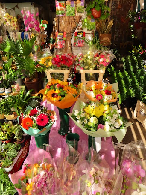 A display of fresh floral bouquets arranged on a pink table, featuring a variety of colorful flowers including bright pink gerbera daisies, yellow sunflowers, and white roses, all wrapped in decorativ